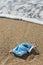 Used surgical mask thrown on the sand of a beach