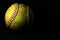 A used yellow softball isolated on a black background.