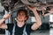 Uses wrench to fix car. Adult man in grey colored uniform works in the automobile salon