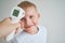 Using infrared thermometer to measure child`s body temperature on a gray background