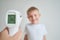 Using infrared thermometer to measure child`s body temperature on a gray background