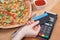 Using payment terminal with contactless credit card for paying in restaurant, finance concept, vegetarian pizza