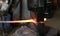 Using pneumatic hammer to shape hot metal. Making the sword out of metal. Side view.