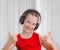 Ð¡ute teen girl listening to music in headphones and showing a thumbs up gesture