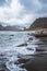 Uttakleiv Beach in Lofoten on a cloudy day with rocks and sandy beach with mountains in the Background.