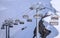 Vacant cableway lift chairs of an empty ski resort at sunny winter day against snowy mountain slopes background