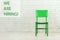 Vacant green wooden chair on white brick wall. We are hiring message