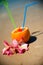 Vacation concept - orange with coctail straw and exotic flowers on the beach