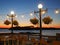 Vacation concept twilight scene with bar chairs around glowing lights at sunset over a lake with and island and jetty in