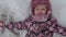 Vacation, game, childhood concept - slo-mo authentic happy preschool toddler baby girl smile lies in snow on back and