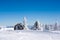 Vacation rural winter background with small wooden alpine house, white pines, fence, snow field, mountains