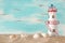 Vacation and summer concept with vintage boat, starfish, lighthouse and seashells over beach sand infront of pastel blue