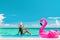 Vacation summer fun woman sunbathing with inflatable pink flamingo pool float by infinity swimming pool. Luxury travel