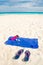 Vacation and summer holidays concept - flip flops, towel, bottled water and bottle of sunscreen oil on beach sand