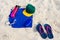 Vacation and summer holidays concept - flip flops, towel, cap, bottled water and bottle of sunscreen oil on beach sand