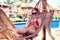 Vacation and technology. Young pretty woman in swimsuit using smartphone laying in hammock beside pool