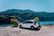 Vacation travel with car concept. Rental hired car in front of amazing bay with turquoise water. Discover Mediterranean Islands.