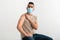 Vaccinated Arab man in face mask showing arm with band aid after covid-19 vaccine shot on white studio background