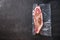Vacuum packed organic beef  top blade steak for sous vide cooking  on black textured background, top view with space for text