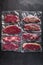 Vacuum packed organic raw beef alternative cuts: top blade, rump, picanha, chuck roll steaks, over black textured background,