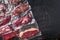 Vacuum packed organic raw beef alternative cuts: top blade, rump, picanha, chuck roll steaks, over black textured background, top