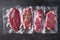 Vacuum packed organic raw beef alternative cuts: top blade, rump, picanha, chuck roll steaks, over black textured background, top
