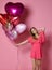 Valentine Beauty girl hold red and pink air balloons laughing on pink background celebrating Valentines Day