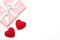 Valentine day idea composition: pink or coral gift box with white ribbon and small red hearts on white background. Top view.