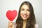 Valentine`s Day. Beautiful young woman holding a paper heart and smile at camera on gray background