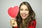 Valentine`s Day. Beautiful young woman in love holding a paper heart and smile at camera on gray background.