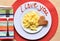 Valentine\'s Day breakfast, I love You scrambled eggs top down view, red background, white plate, fork on left