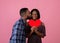 Valentine& x27;s Day celebration. Handsome black guy kissing his beautiful girlfriend with red heart on pink background