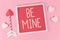 Valentine`s Day composition with picture frame with text `Be Mine`, cupid love arrows, and white hearts on pink background