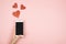 Valentine`s day concept, mobile phone in hand screen with red hearts on pink background. Love in social media