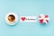 Valentine`s Day holiday card. Red gift box, heart and cup of coffee on pastel blue background. Valentines day festive concept