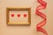 Valentine`s day or Wedding romantic concept. Twisted decorative ribbon and golden photo frame with red hearts on beige background