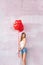 Valentine smiling girl holding red air balloons, posing in pajamas on the pink wall. Beautiful Happy Young woman