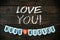 Valentines crafting. LOVE YOU chalk lettering. Banner HUGS and KISSES, red paper heart on dark barn wood background. Space for