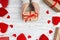 Valentines Day background. Female hands holding Valentines day gift above wooden table with red hearts. Top view. Xmas gift wrappi