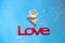 Valentines day card with  figurine of little Cupid holding heart, love angel and word Love  on blue background.