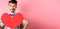 Valentines day concept. Cute boyfriend looking at big red heart, waiting for lover on romantic date, pink background