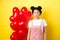 Valentines day concept. Sad and gloomy asian woman in makeup, frowning upset, standing near red hearts balloons and