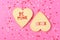 Valentines Day Concept: Two Heart shaped sugar cookies on pink  Be Mine and XOXO written in icing, surrounded by heart shaped