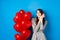 Valentines day. Dreamy romantic woman close eyes and imaging lovely date, standing near heart balloons and smiling, blue