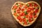 Valentines Day food. Heart shapped pepperoni pizza with green basil,  top view