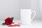 Valentines day mug, cup on the wooden table and white background with red rose and red valentine envelope