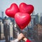 Valentines day in the New York city. man and woman hands holding three red balloons in form of heart over Manhattan