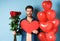Valentines day romance. Young man with bouquet of red roses and heart balloons smiling, bring presents for lover on
