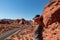 Valley of Fire - Woman standing on endless winding empty Mouse tank road through canyons of red Aztec Sandstone Rock f