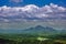 In the valley there is a green forest, In the distance are the silhouettes of mountains.